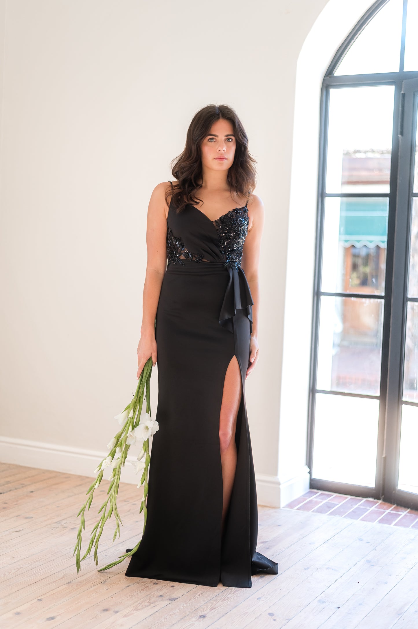 Woman in a black bridesmaid dress featuring thin straps, a thigh slit and beaded lace applique on bodice.