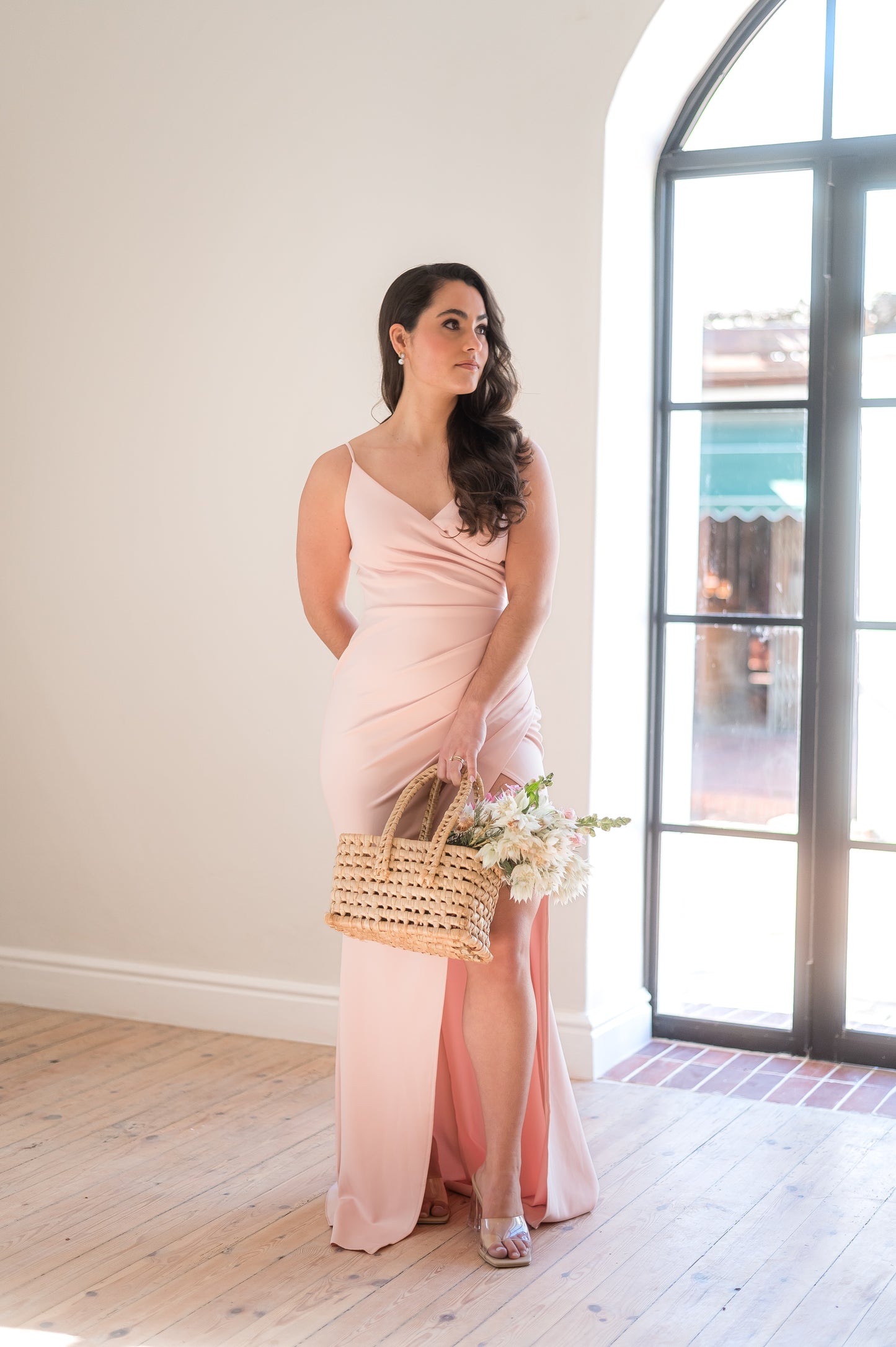 Woman standing in a dusty pink bridesmaid dress featuring thin straps, a V-neck,
Rouging over tummy and a Cross-over slit.