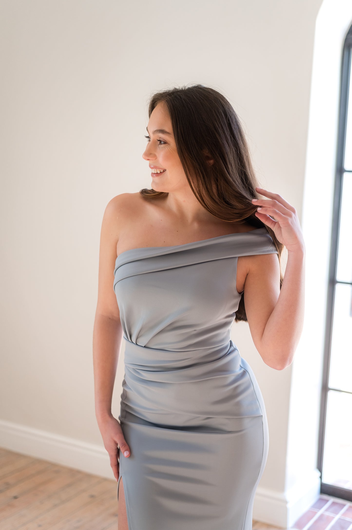 Woman in a sage one-shoulder bridesmaid dress with rouging and a thigh slit.