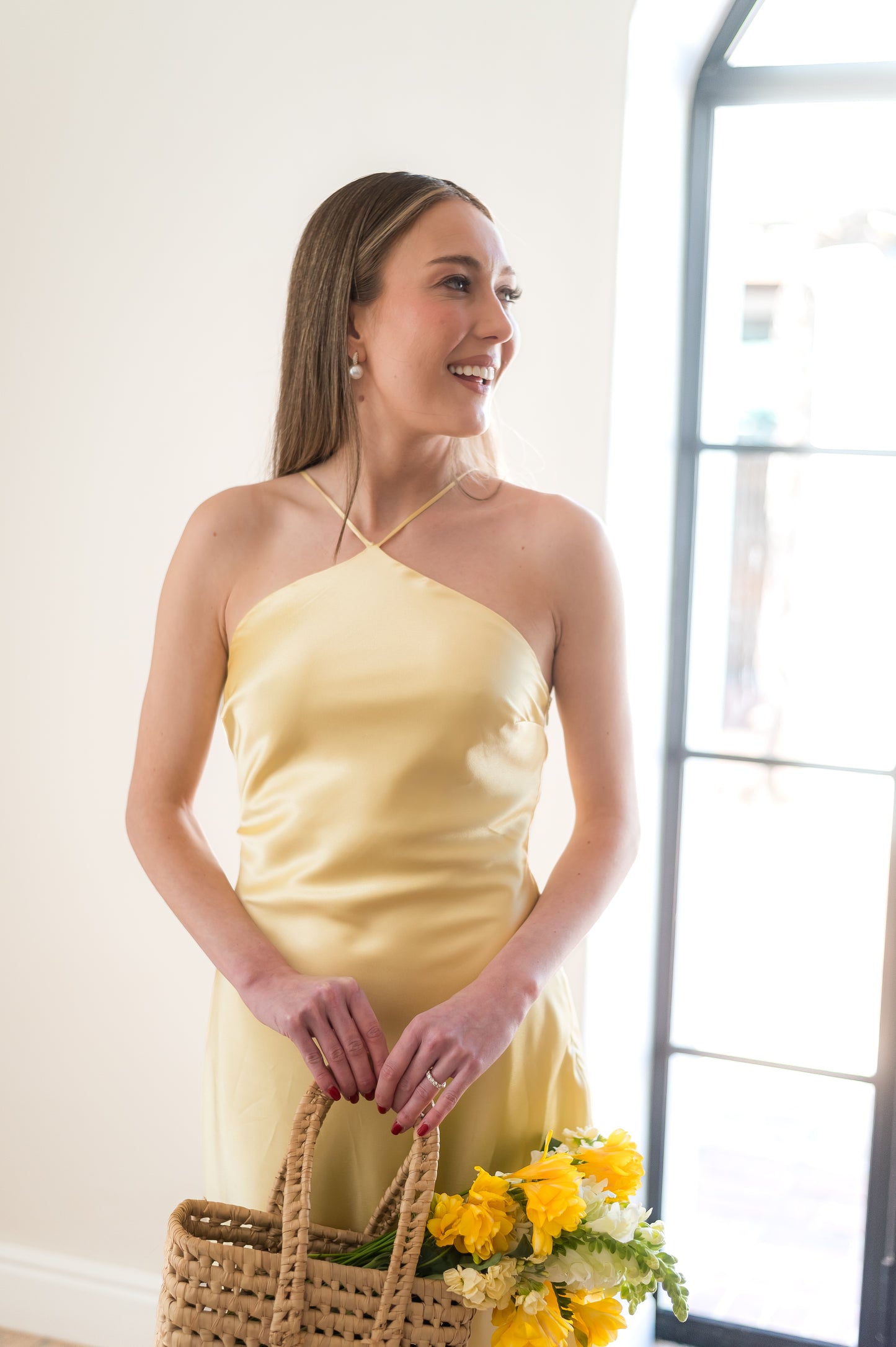 Woman in a butter yellow halter neck dress holding flowers and a woven basket.