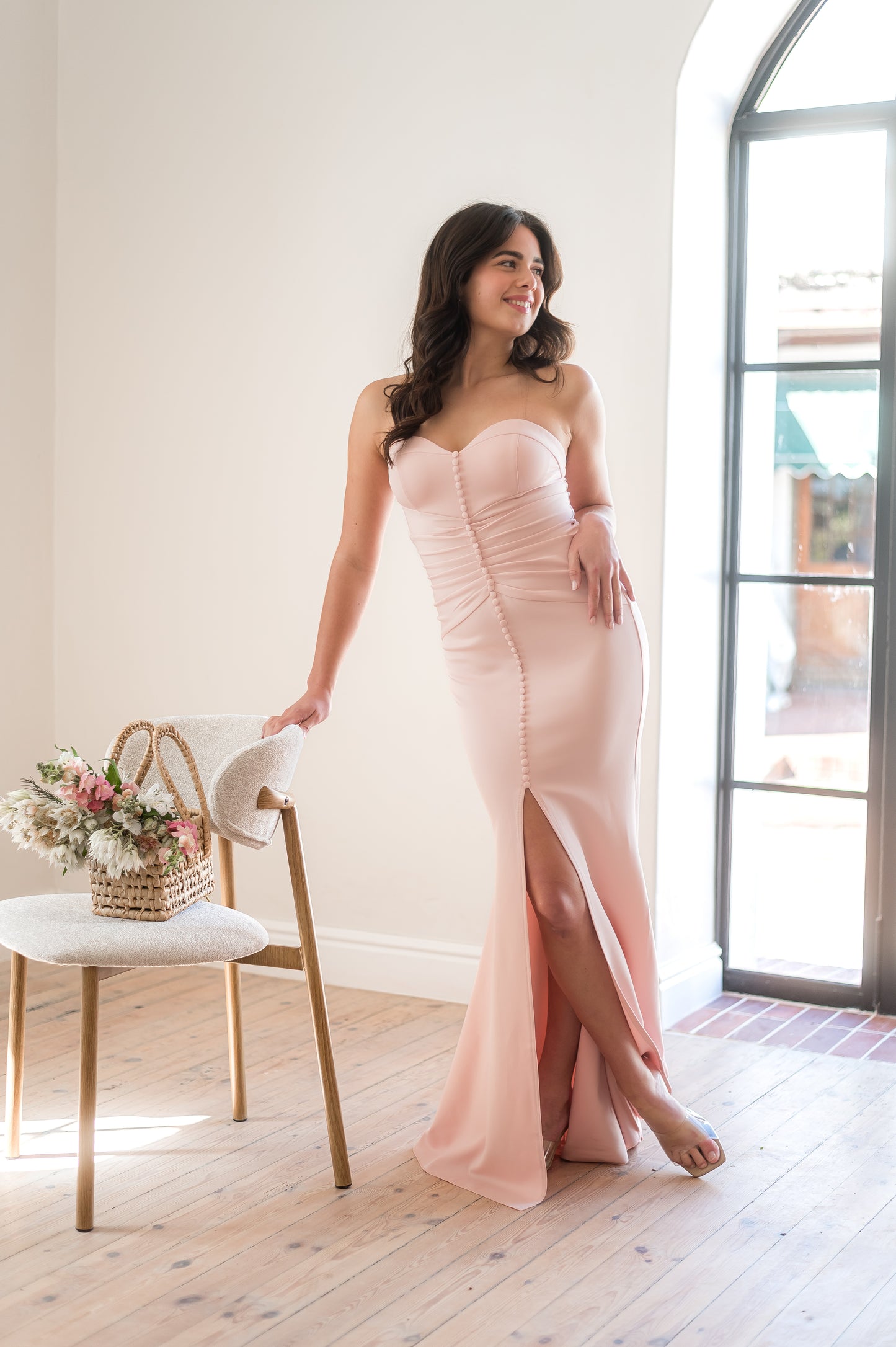 Woman in a strapless dusty pink bridesmaid dress featuring a centre slit, rouging over the tummy and buttons from the bust to the slit .