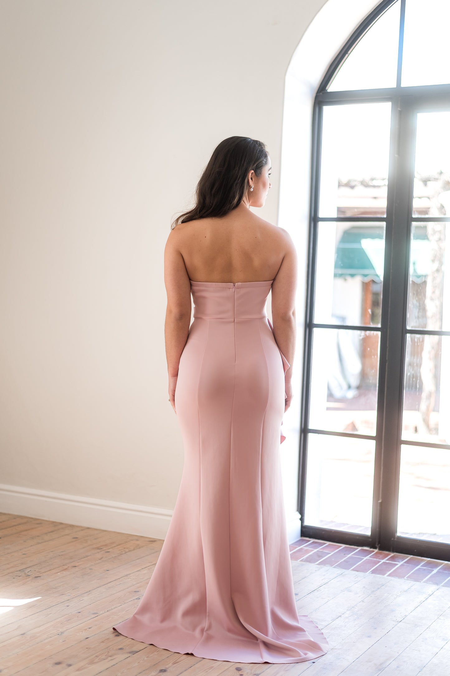 Woman standing in a dusty pink, strapless bridesmaid dress from the back.