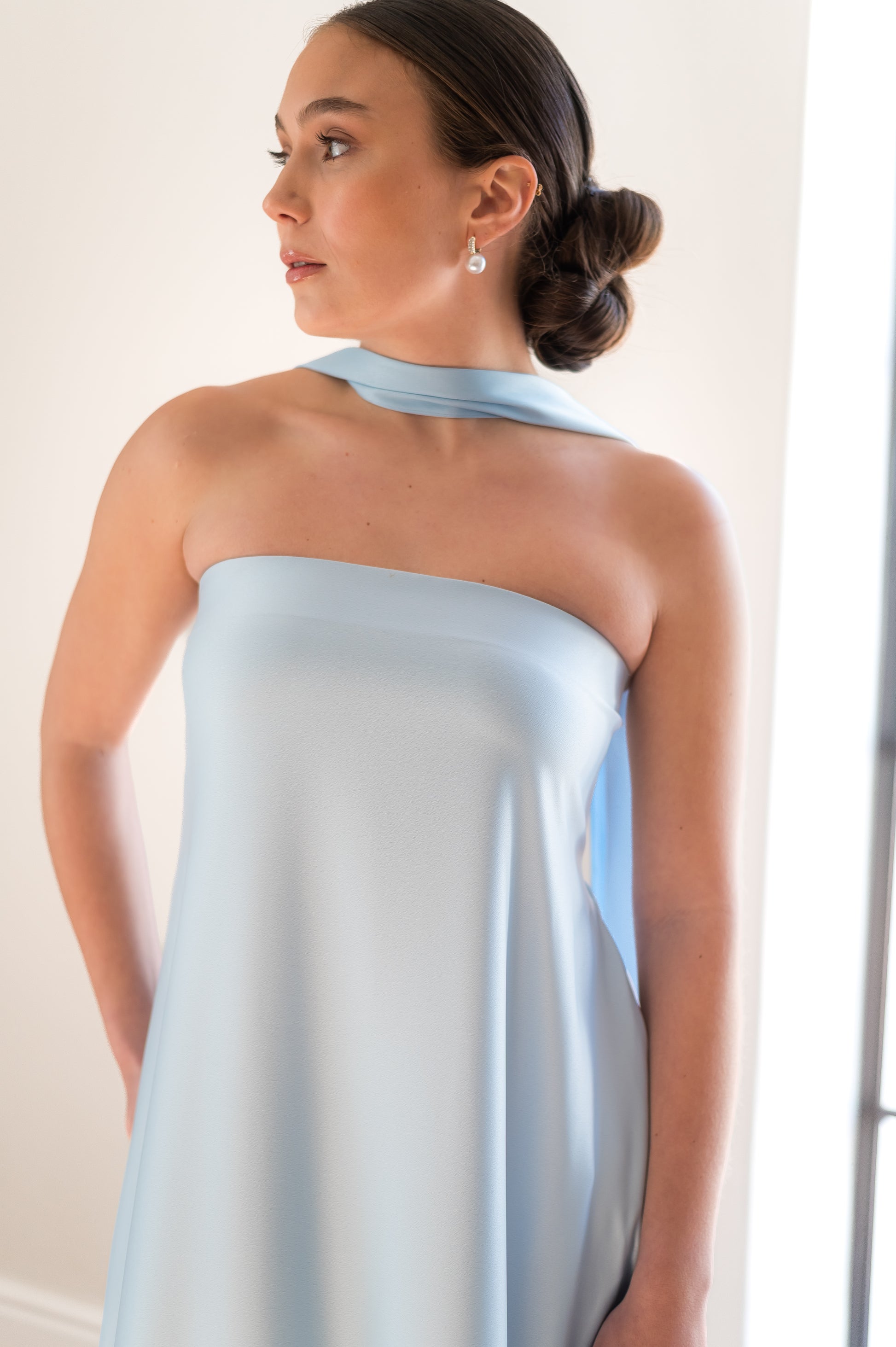 Woman wearing a light blue column dress with a neck scarf against a neutral background