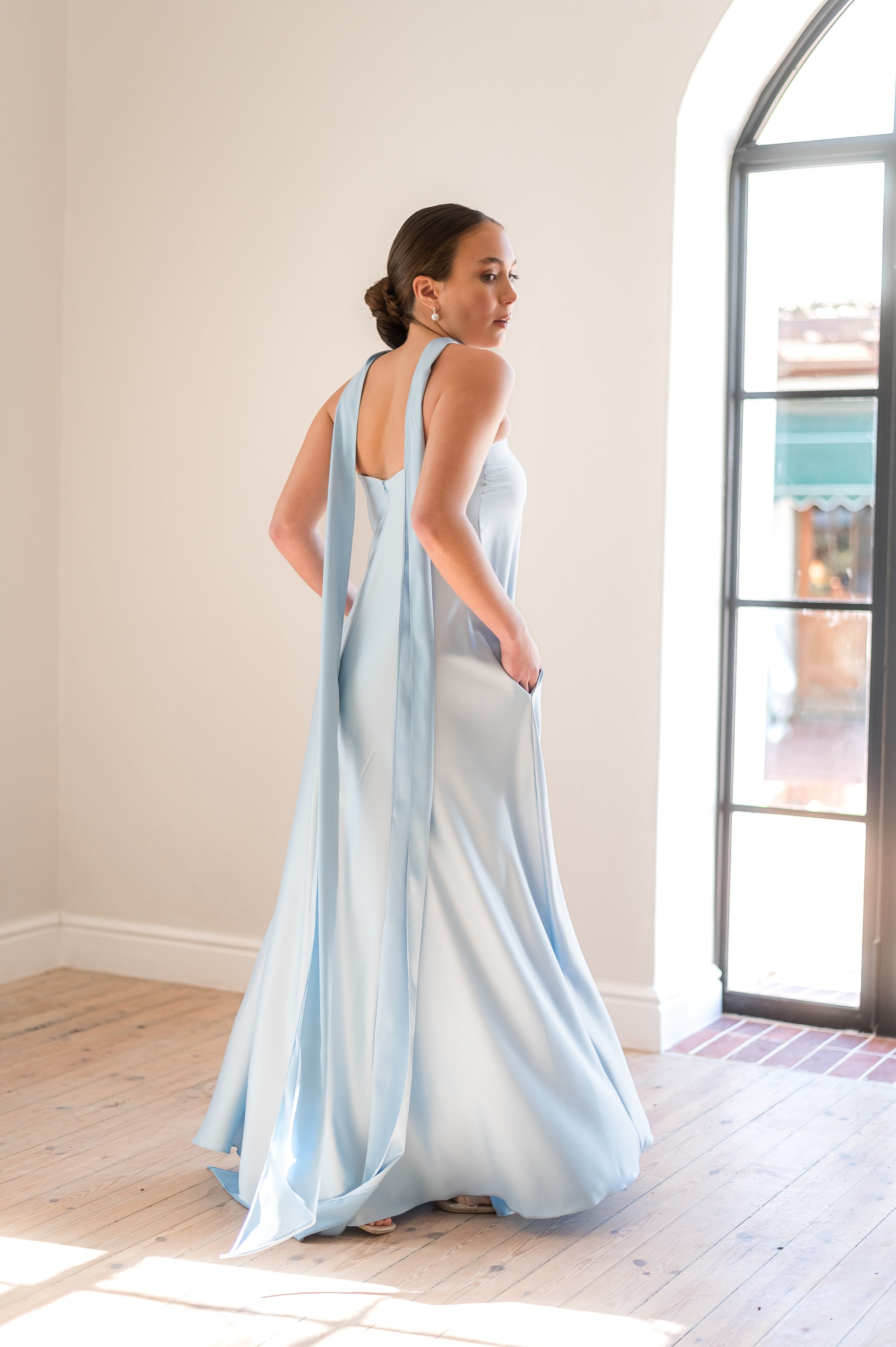 Woman in a flowy light blue strapless dress with a neck scarf hanging behind her. 