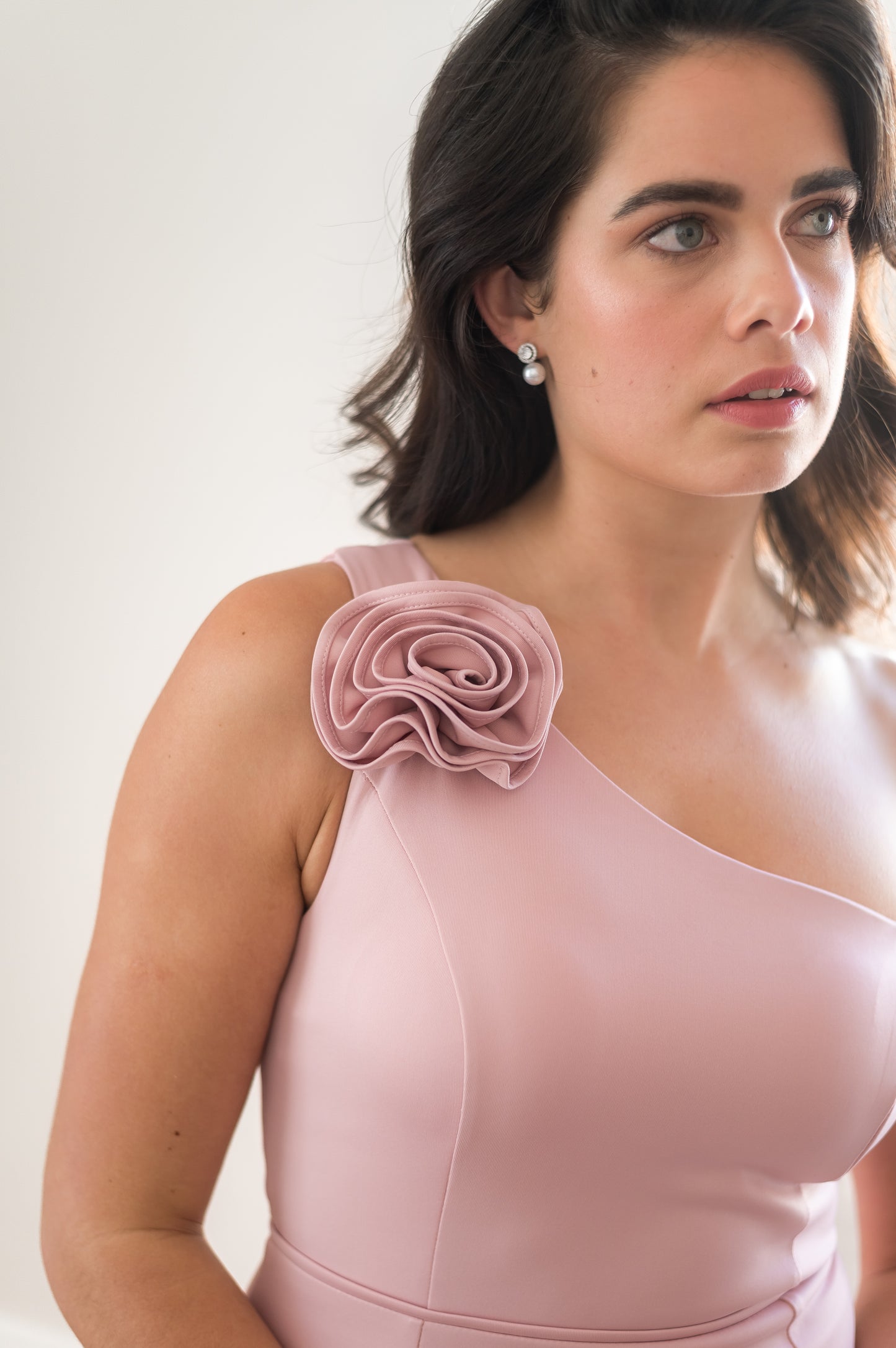 Woman wearing a pink one-shoulder bridesmaid dress with a floral detail on a white background