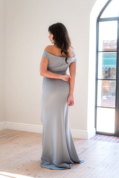 Woman in a  Sage off-shoulder bridesmaid dress from the back in a light filled room. 