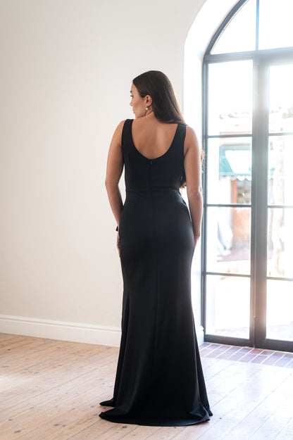 Woman in a black bridesmaid dress from the back featuring a rounded back and  broad straps.