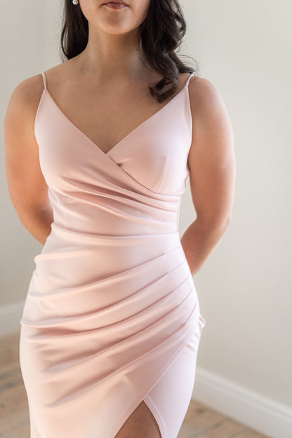 Close up of a dusty pink bridesmaid dress featuring thin straps, a V-neck, 
Rouging over tummy and a Cross-over slit.