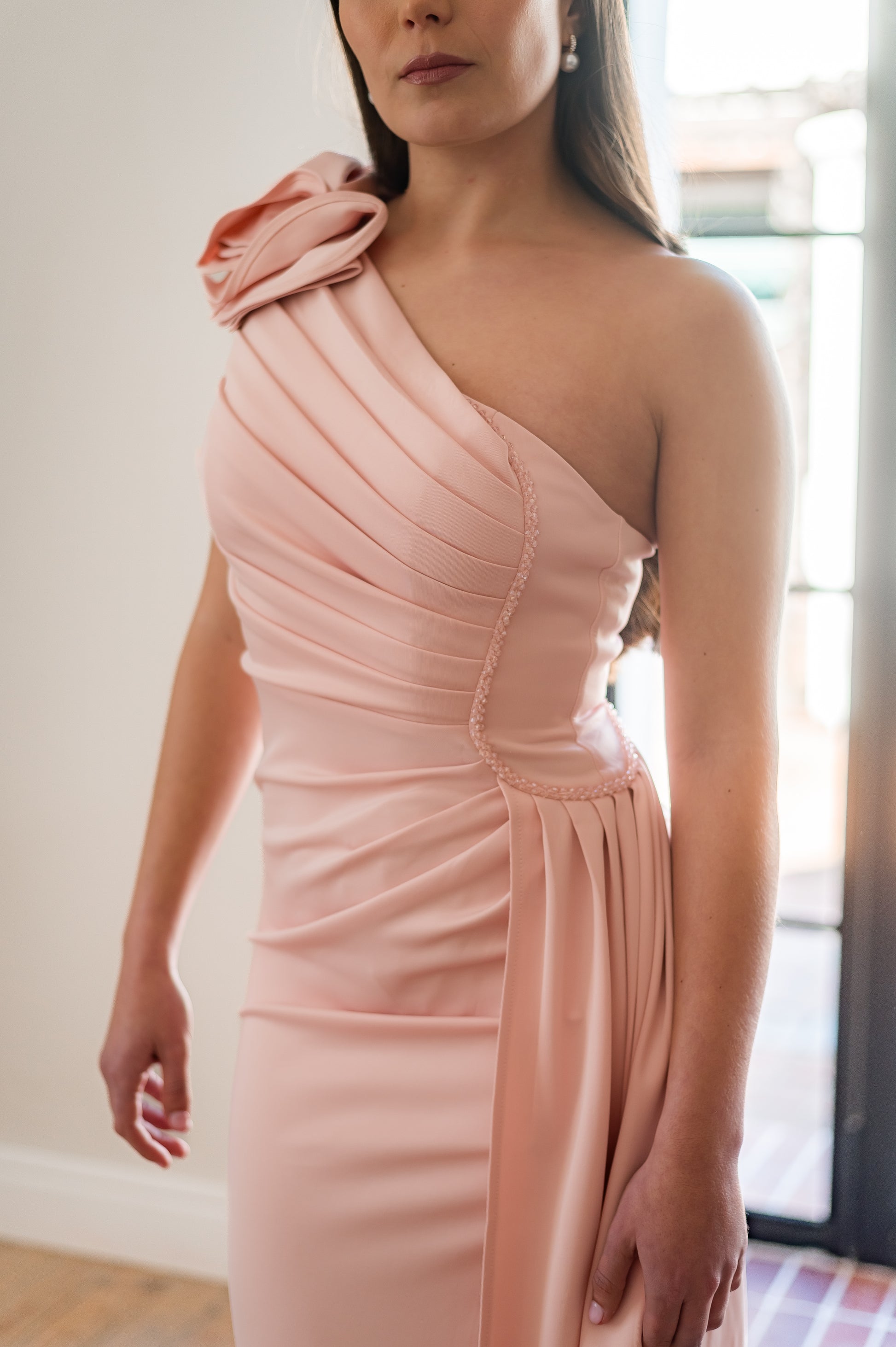 Woman wearing a pink one-shoulder, 3D flower detail  bridesmaids dress with beading on the one side of the waist. 
