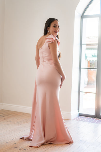 Woman wearing a pink one-shoulder, 3D flower detail  bridesmaids dress with beading on the one side of the waist. 